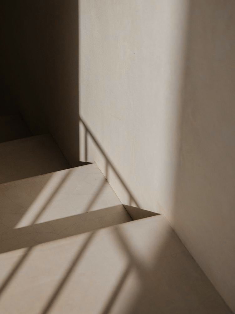 Luz natural proyectando sombras suaves sobre una escalera y una pared minimalista, evocando el espacio de calma del consultorio
